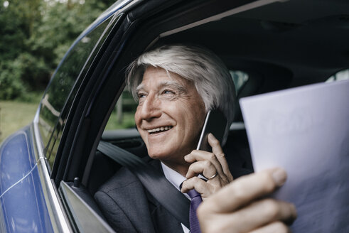 Smiling senior businessman with documents on the phone in a car - KNSF01030