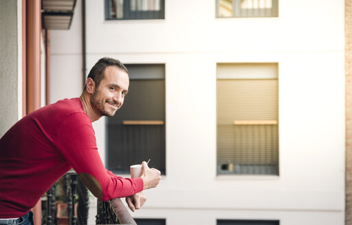 Portrait of smiling man standing on balcony with coffee mug - EPF00329