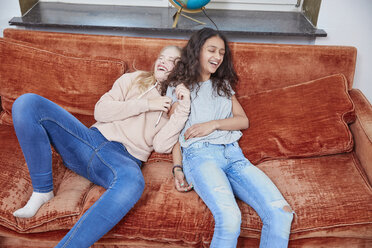 Zwei lachende Mädchen entspannen sich auf der Couch - RHF01813