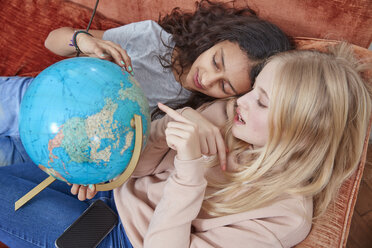 Two girls lying on couch pointing at globe - RHF01821