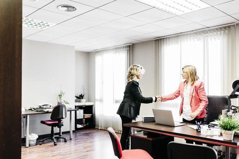 Zwei Geschäftsfrauen beim Händeschütteln im Büro, lizenzfreies Stockfoto