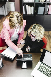 Two businesswomen using laptop at desk in office - JRFF01192