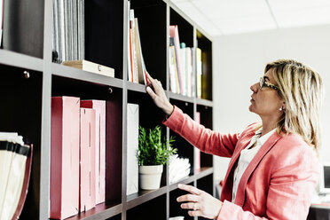 Geschäftsfrau betrachtet Dokumente im Bücherregal - JRFF01202