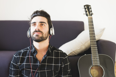 Junger Mann zu Hause mit Kopfhörern neben einer Gitarre, lizenzfreies Stockfoto