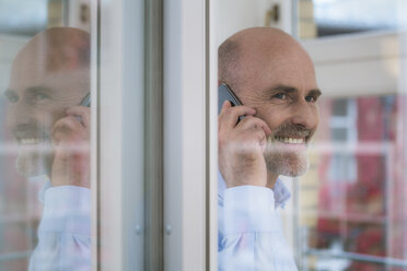 Lächelnder Geschäftsmann mit Mobiltelefon am Fenster - FKF02128