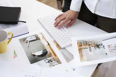 Nahaufnahme einer Frau, die eine Fotografie hält und eine Computertastatur im Büro benutzt, lizenzfreies Stockfoto