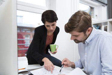 Colleagues working together at desk in office - FKF02150