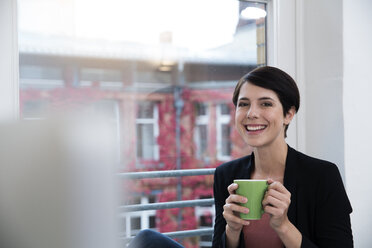 Porträt einer lächelnden Frau, die eine Tasse Kaffee am Fenster hält - FKF02151