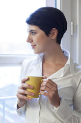 Frau hält eine Tasse Kaffee und schaut aus dem Fenster - FKF02152
