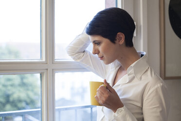 Woman holding cup of coffee looking out of window - FKF02153
