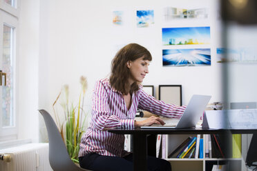 Lächelnde Frau mit Laptop im Büro - FKF02169