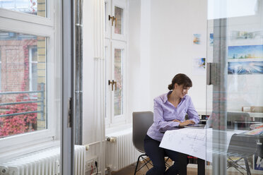 Smiling woman using laptop in office - FKF02170