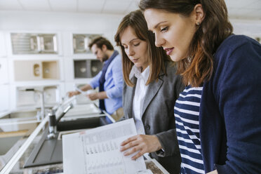 Customers consulting saleswoman in shop for kitchen sinks - ZEDF00517