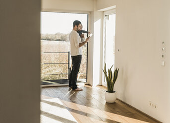 Father standing at home, carrying baby son and reading text messages - UUF09870