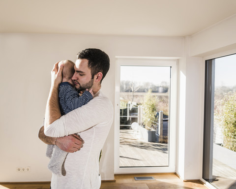 Vater hält und umarmt seinen kleinen Sohn, der in einem gemütlichen Haus steht, lizenzfreies Stockfoto
