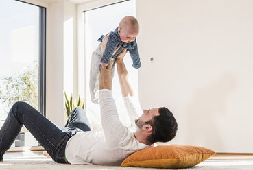 Father playing with baby son, lying on carpet - UUF09878