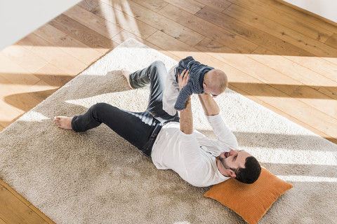 Vater spielt mit seinem kleinen Sohn, der auf dem Teppich liegt, lizenzfreies Stockfoto
