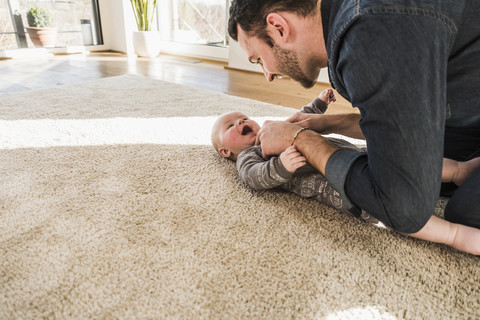 Vater und kleiner Sohn spielen auf dem Teppich zu Hause, lizenzfreies Stockfoto