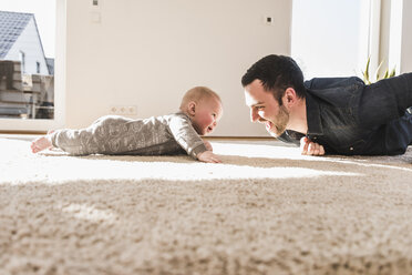 Vater und kleiner Sohn spielen krabbelnd auf Teppich - UUF09900