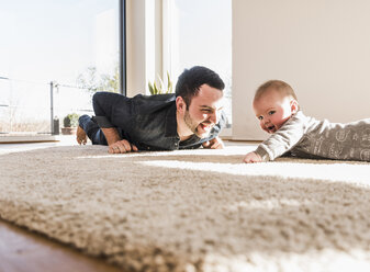 Vater und kleiner Sohn spielen krabbelnd auf Teppich - UUF09901