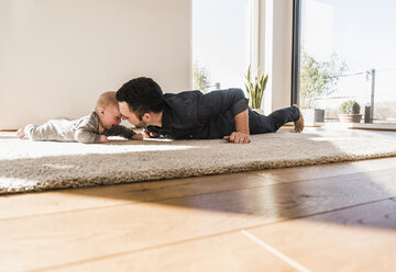 Father and baby son playing crawling on carpet - UUF09902