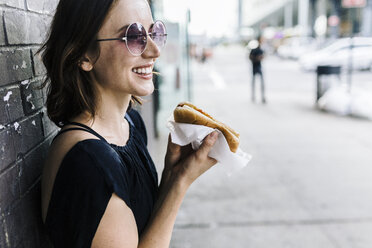 Smiling woman with Hot Dog leaning against wall - GIOF01867