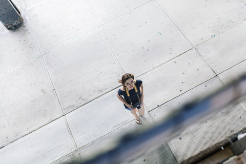 Frau mit Kamera, die den Platz überquert und nach oben schaut, lizenzfreies Stockfoto