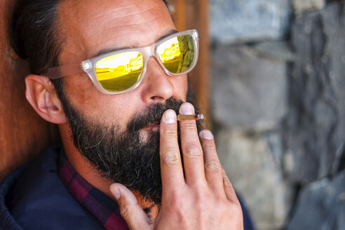 Porträt eines Mannes mit verspiegelter Sonnenbrille, der Zigarillo raucht - SIPF01404
