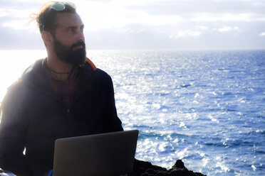 Portrait of man with laptop at backlight in front of the sea - SIPF01406