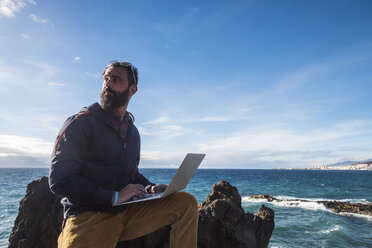 Spanien, Teneriffa, Porträt eines Mannes mit Laptop vor dem Meer - SIPF01411