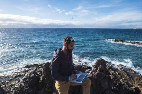 Spanien, Teneriffa, Mann mit Laptop vor dem Meer, lizenzfreies Stockfoto