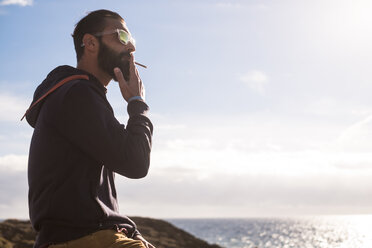 Porträt eines Mannes, der Zigarillo raucht und auf das Meer blickt - SIPF01415