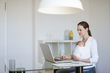 Mother with baby girl in sling working from home - DIGF01506