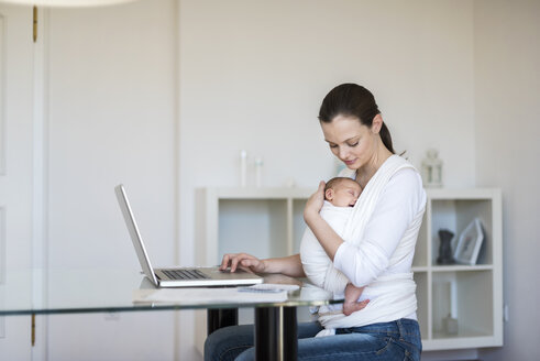 Mutter mit Baby im Tragetuch arbeitet von zu Hause aus - DIGF01507