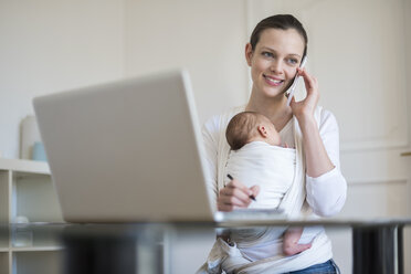 Mutter mit Baby im Tragetuch arbeitet von zu Hause aus - DIGF01510