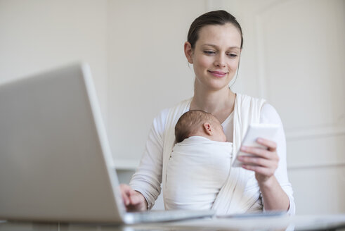 Mutter mit Baby im Tragetuch arbeitet von zu Hause aus - DIGF01511