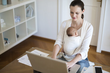 Mother with baby girl in sling working from home - DIGF01517