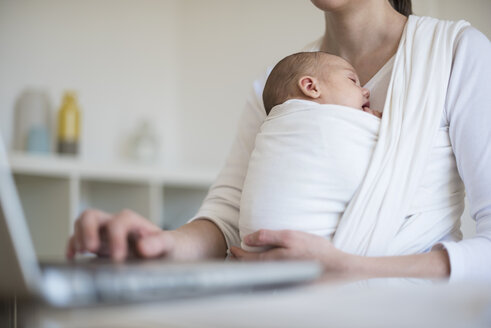 Mutter mit Baby im Tragetuch arbeitet von zu Hause aus - DIGF01518