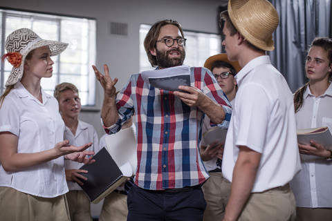 Schauspiellehrerin führt Schüler an, die Requisiten tragen, lizenzfreies Stockfoto