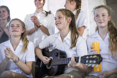 Gymnasiastin spielt draußen Gitarre mit einer Gruppe von Schulfreunden, lizenzfreies Stockfoto