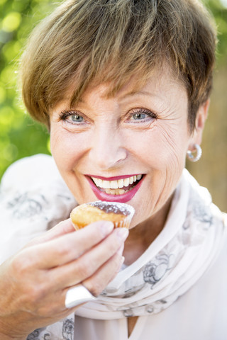 Porträt einer lächelnden älteren Frau, die einen Muffin im Freien isst, lizenzfreies Stockfoto