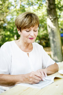 Ältere Frau löst ein Kreuzworträtsel im Freien - WESTF22678