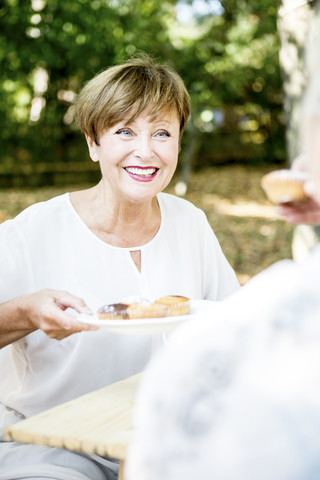 Lächelnde ältere Frau bietet Muffins an, lizenzfreies Stockfoto