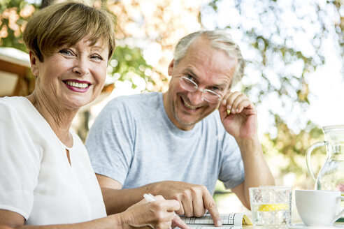 Smiling senior couple outdoors doing crossword puzzle together - WESTF22700