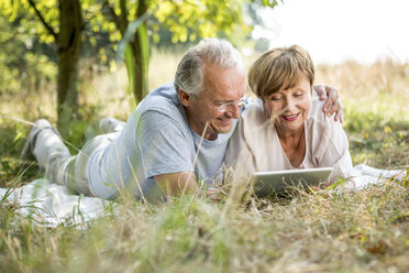 Glückliches Seniorenpaar mit Tablet auf einer Wiese liegend - WESTF22718