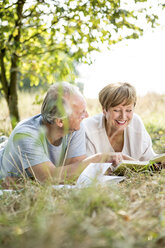 Glückliches Seniorenpaar mit Buch auf der Wiese liegend - WESTF22721