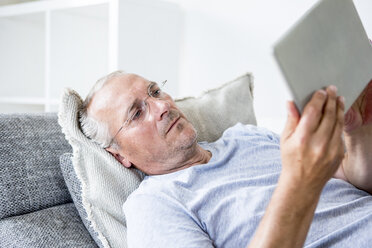 Älterer Mann zu Hause auf der Couch liegend mit digitalem Tablet - WESTF22727