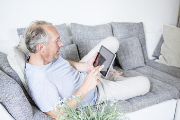 Älterer Mann zu Hause auf der Couch liegend mit digitalem Tablet - WESTF22728