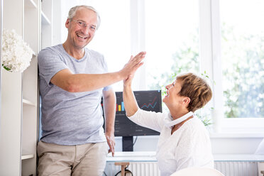 Happy senior couple high fiving in front of computer screen with charts - WESTF22737