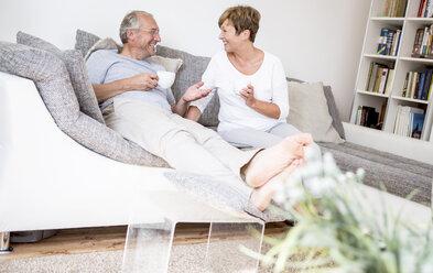 Glückliches älteres Paar sitzt zu Hause auf der Couch und trinkt Kaffee - WESTF22742